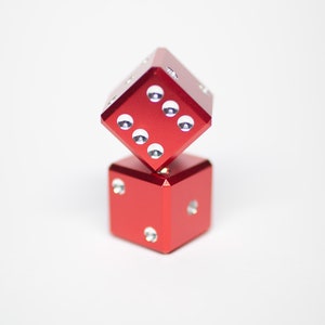 Puede incluir: Dos dados de metal rojo con puntos blancos apilados uno encima del otro.