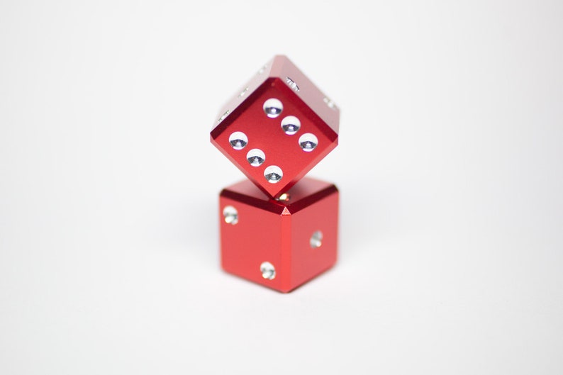 Puede incluir: Dos dados de metal rojo con puntos blancos apilados uno encima del otro.