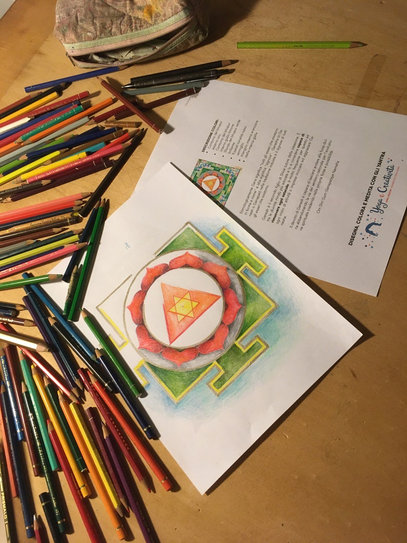 May include: A drawing of a mandala with a red triangle in the center, surrounded by a green square and a blue circle. The drawing is on a white sheet of paper and there are colored pencils on the table.
