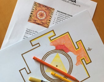 May include: A detailed illustration of a Yantra di Durga, with text in Italian. The image includes a geometric design with orange, yellow, and brown colors. Colored pencils and a gold marker are placed on the paper, suggesting an art project.