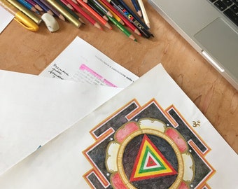 May include: A black and white mandala with a red, yellow, green, and white triangle in the center. The mandala is surrounded by a white circle with a gold border. The mandala is on a white sheet of paper with the text "DISEGNA, COLORA E MEDITA CON G" and "Yoga e Cre" in black and white.