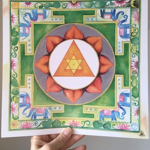 Può includere: Un dipinto ad acquerello di un mandala con sfondo verde, un triangolo arancione e giallo al centro ed elefanti blu negli angoli.