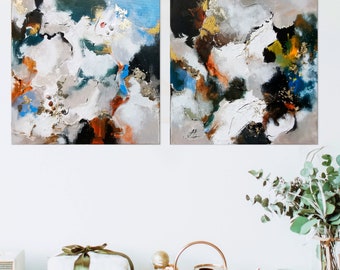 May include: Two abstract paintings with a white background and splashes of blue, green, gold, and brown paint. The paintings are hanging on a white wall.
