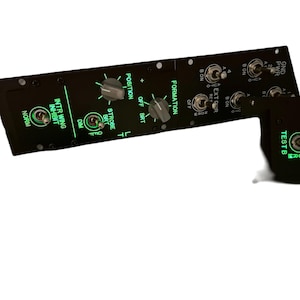 May include: Black control panel with green illuminated text and switches. The panel includes labels such as "INTR WING INHIBIT," "STROBE BRT," and "FORMATION." It features toggle switches and rotary dials for various functions.