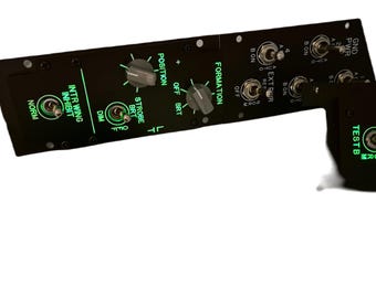 May include: Black control panel with green illuminated text and switches. The panel includes labels such as "INTR WING INHIBIT," "STROBE BRT," and "FORMATION." It features toggle switches and rotary dials for various functions.
