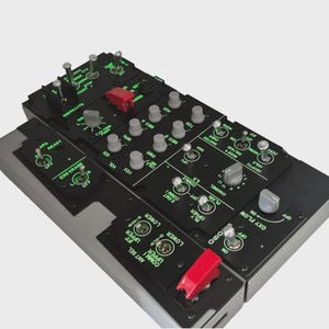 Puede incluir: Un panel de control negro detallado con numerosos interruptores, perillas y botones, etiquetados con texto blanco. Cuenta con interruptores basculantes rojos y grises y diales giratorios. El panel es probablemente para una aeronave o simulador.