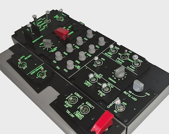 May include: A detailed close-up of a black control panel with various switches, knobs, and buttons. The panel has green illuminated text and red and gray accents. The panel is likely for an aircraft or simulator.