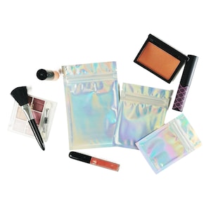 May include: Four iridescent holographic zippered pouches in various sizes, a makeup brush, a lipstick tube, a compact with a brown eyeshadow, and a black eyeliner pencil.