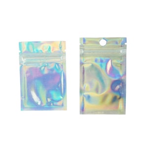 Puede incluir: Dos bolsas holográficas iridiscentes con cierre zip. Las bolsas tienen forma rectangular con cierre de cremallera transparente y resellable. Una bolsa tiene un pequeño agujero en la parte superior. Reflejan azules, verdes y morados, creando un efecto brillante.