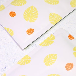 May include: Two white mailing envelopes with a repeating pattern of yellow monstera leaves and orange circles.