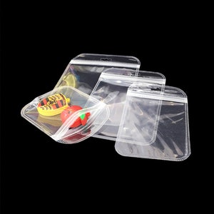 May include: Three clear plastic zippered bags with a hanging hole at the top. The bags are different sizes and are lying flat on a black surface.