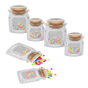 May include: Clear glass jars with cork stoppers, filled with colorful candies. Some jars are upright, while others are tipped over, spilling the candies. The candies are various colors, including red, yellow, blue, and green.