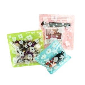 Può includere: Tre sacchetti di plastica trasparenti con cerniera a zip con diversi motivi floreali e di uccelli. I sacchetti sono vuoti, ma uno contiene una piccola palette di trucco.