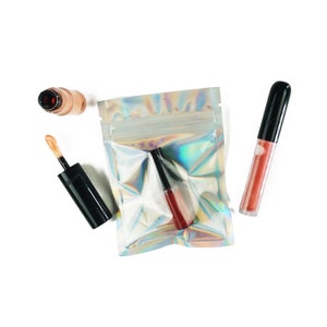 May include: Three small bottles of liquid makeup in a clear iridescent plastic bag. The bottles are black with clear tops and contain a light brown, a light pink, and a dark red liquid.