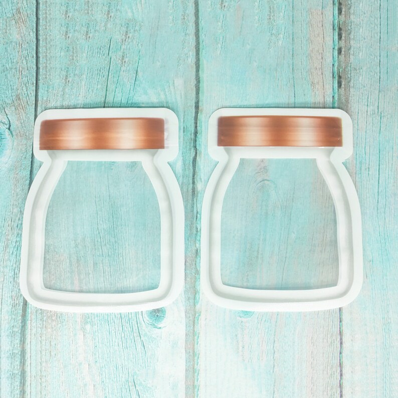 May include: Two white cookie cutters shaped like jars with a copper-colored lid. The cookie cutters are on a light blue wooden background.