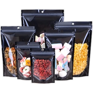 May include: A collection of black, resealable stand-up pouches with clear windows, showcasing various food items. The pouches contain pasta, candies, dried berries, and cereal. Each pouch has a small hole near the top for hanging.