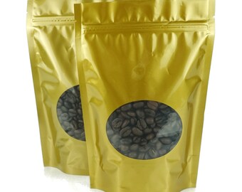 May include: Two gold stand-up pouches with a clear window showing dark roasted coffee beans inside.