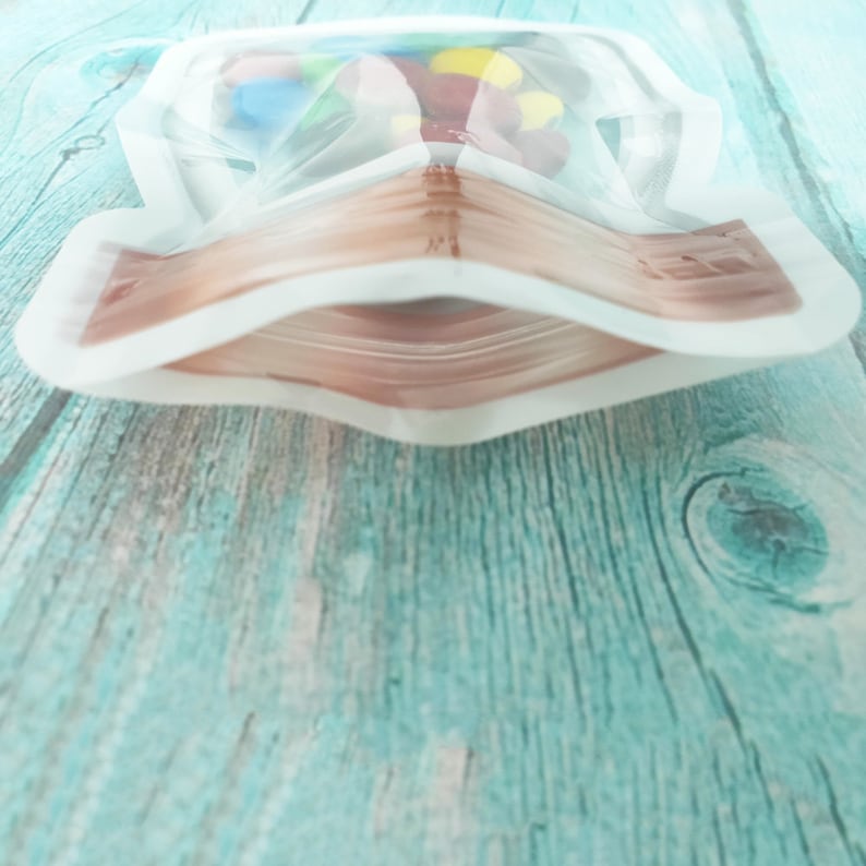May include: A clear plastic bag with a zipper closure. The bag is filled with colorful candy. The bag is lying on a light blue wooden surface.