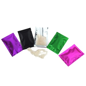 May include: Five small, colorful, foil pouches with a white powder spilling out of one of the pouches. The pouches are purple, black, silver, green, and pink.