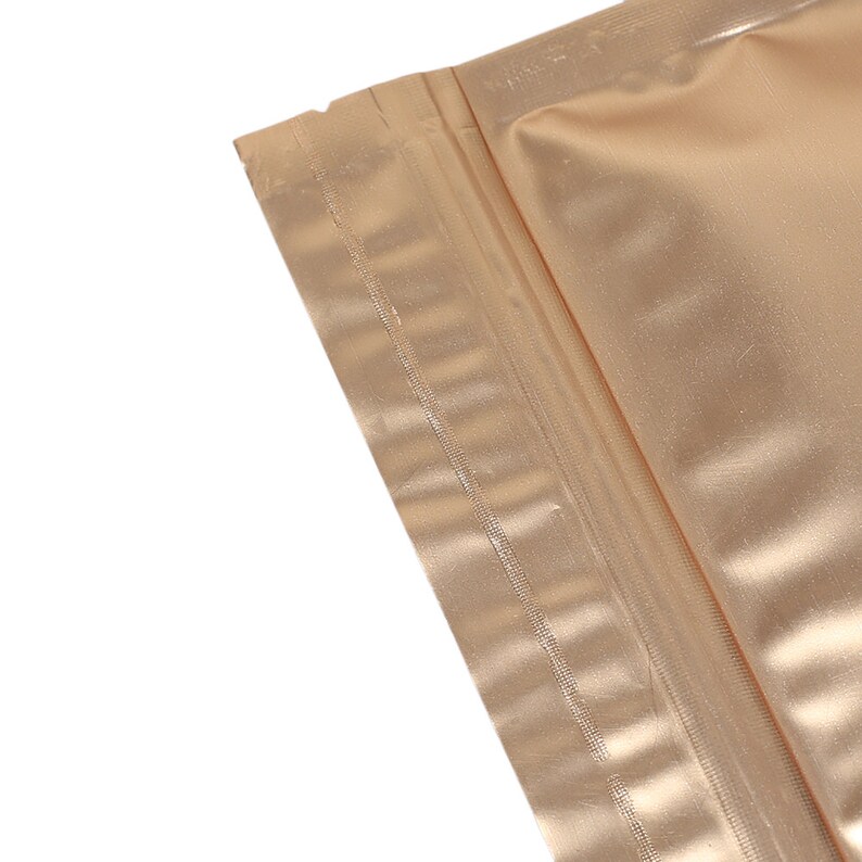 May include: Close-up of a gold-colored zipper seal on a pouch. The zipper is closed and the pouch is made of a shiny, metallic material.