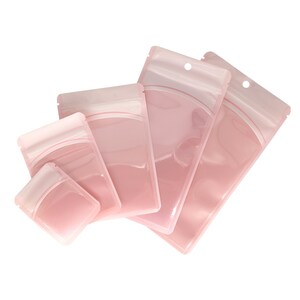 Op de afbeelding: Vier roze plastic hersluitbare zakken met een ritssluiting. De zakken zijn van verschillende grootte en zijn op elkaar gestapeld.