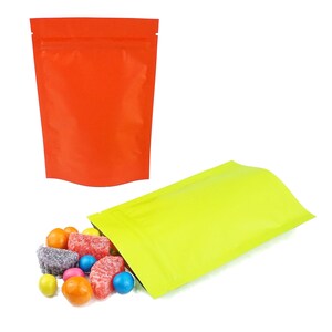 May include: Two stand-up pouches, one red and one green, with a pile of colorful candies spilling out of the green pouch.