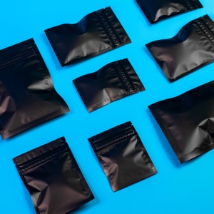 May include: A flat lay of nine black zippered pouches on a bright blue background. The pouches are various sizes and are arranged in a staggered pattern.