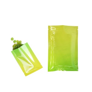 May include: Two clear plastic pouches with a yellow to green gradient. The pouches are lying flat on a white background. One pouch is filled with small green and white round candies.