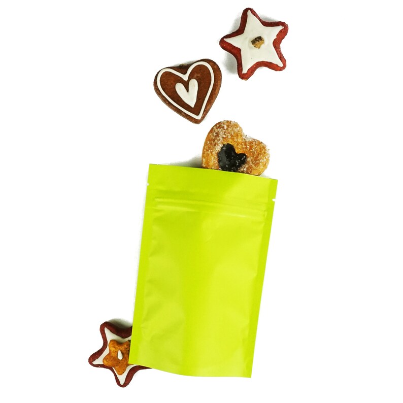 May include: A bright green stand-up pouch with a zipper closure. The pouch is empty, but there are three gingerbread cookies in the shape of a star and two hearts scattered around it.
