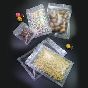 May include: Four clear plastic stand-up pouches with resealable zippers. The pouches are filled with various items, including colorful sprinkles, acorns, pasta, and dried flowers.