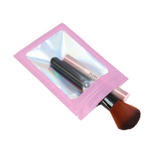 May include: Pink iridescent zippered pouch with a clear window, showing two makeup brushes inside. The brushes are black with brown bristles.