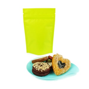 May include: A bright green resealable pouch with a variety of cookies on a blue plate. The cookies include a heart-shaped cookie with a black center, a round cookie with white frosting, and a round cookie with brown frosting and sprinkles.