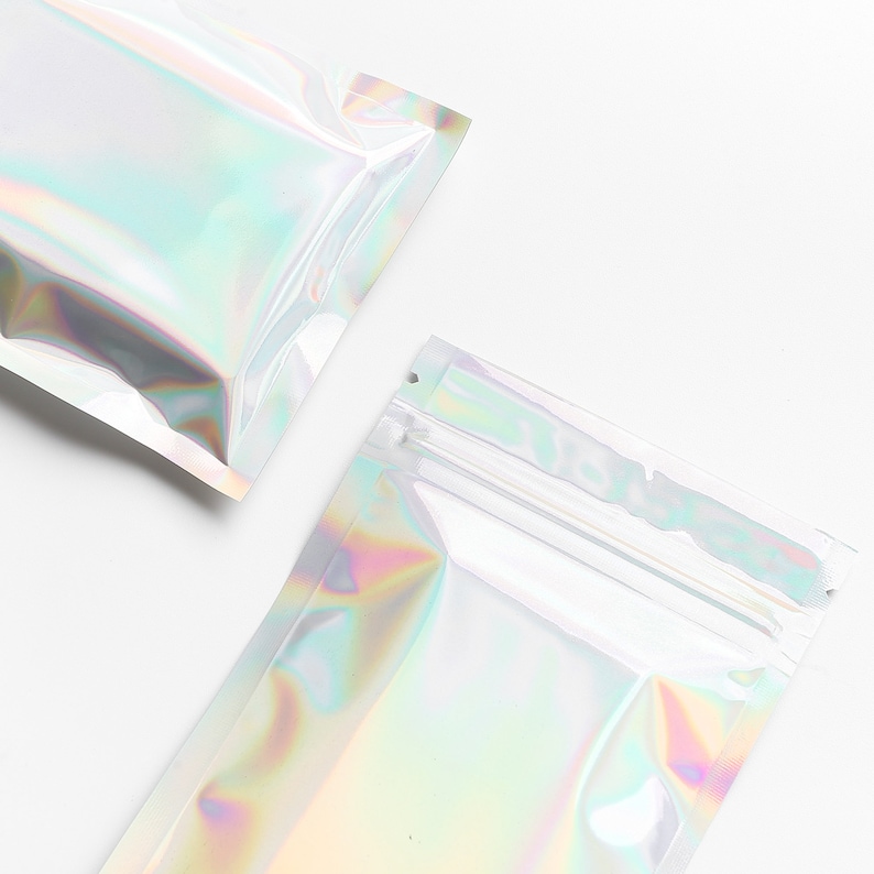 May include: Two iridescent clear plastic zippered bags on a white background. The bags are lying flat and are empty.