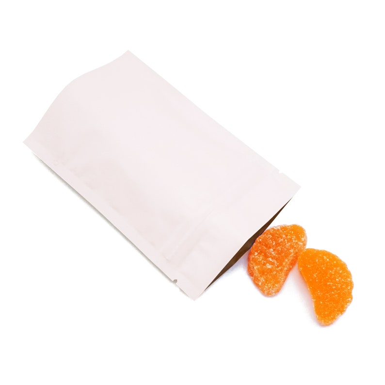 May include: A white stand-up pouch with two orange gummy candies spilling out of the top.