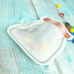 May include: A clear plastic bag shaped like a jar with a brown top. The bag is filled with colorful candies.