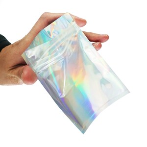 May include: A clear iridescent plastic bag with a zipper closure. The bag is made of a holographic material that reflects light in a rainbow of colors.