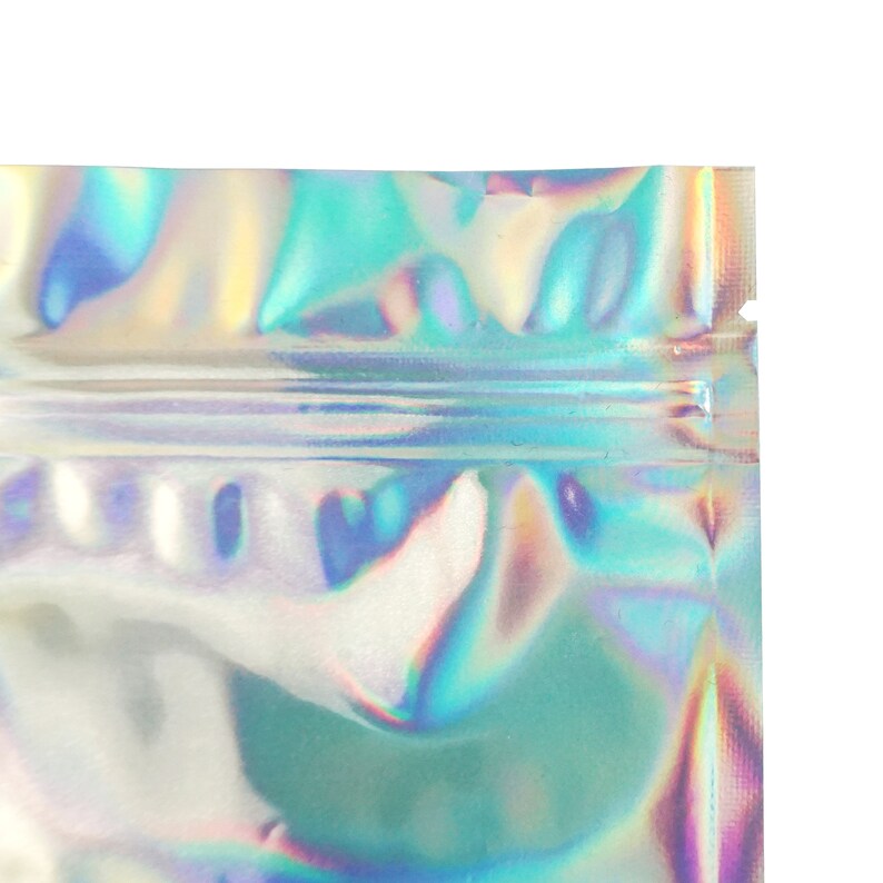 May include: A close-up of a silver iridescent zippered pouch with a holographic finish. The pouch is made of a thin, flexible material and has a smooth, shiny surface.