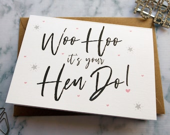 May include: A white card with the text "Woo Hoo it's your Hen Do!" in black script. The card is decorated with pink hearts and silver stars.