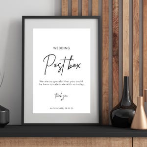 Puede incluir: Un cartel negro enmarcado con texto blanco que dice "Wedding Postbox" y "We are so grateful that you could be here to celebrate with us today. Thank you. Katie & Sam | 20.03.25".