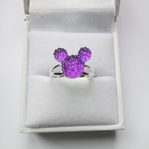 K&ouml;nnte beinhalten: Ein silberner Ring mit einem funkelnden lila Mickey Mouse Kopfdesign.