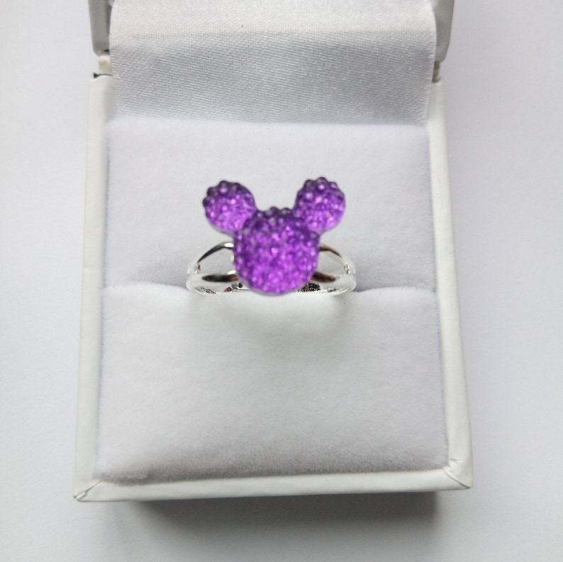 K&ouml;nnte beinhalten: Ein silberner Ring mit einem funkelnden lila Mickey Mouse Kopfdesign.