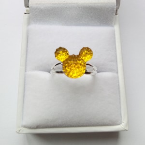 K&ouml;nnte beinhalten: Ein silberner Ring mit einem gelben, glitzernden Mickey Mouse Kopfdesign.