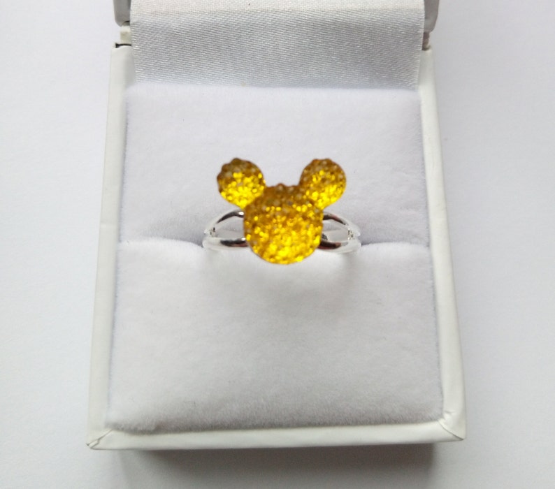 May include: A silver ring with a yellow, sparkly Mickey Mouse head design.
