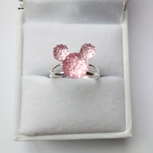 K&ouml;nnte beinhalten: Ein silberner Ring mit einem pinkfarbenen Glitzer-Mickey-Mouse-Kopf-Design.
