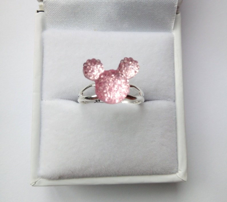 K&ouml;nnte beinhalten: Ein silberner Ring mit einem pinkfarbenen Glitzer-Mickey-Mouse-Kopf-Design.