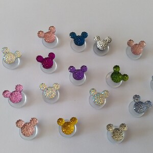 May include: Assortment of 15 sparkly, colorful Mickey Mouse ears with rhinestones. The ears are attached to a clear adhesive backing.