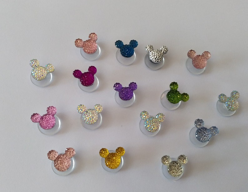 May include: Assortment of 15 sparkly, colorful Mickey Mouse ears with rhinestones. The ears are attached to a clear adhesive backing.