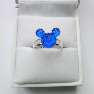 K&ouml;nnte beinhalten: Ein silberner Ring mit einem blauen Kristall-Mickey-Mouse-Kopf-Design.