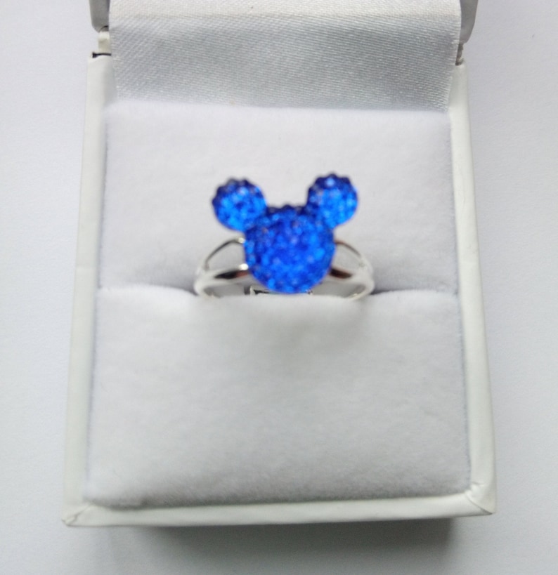 K&ouml;nnte beinhalten: Ein silberner Ring mit einem blauen Kristall-Mickey-Mouse-Kopf-Design.
