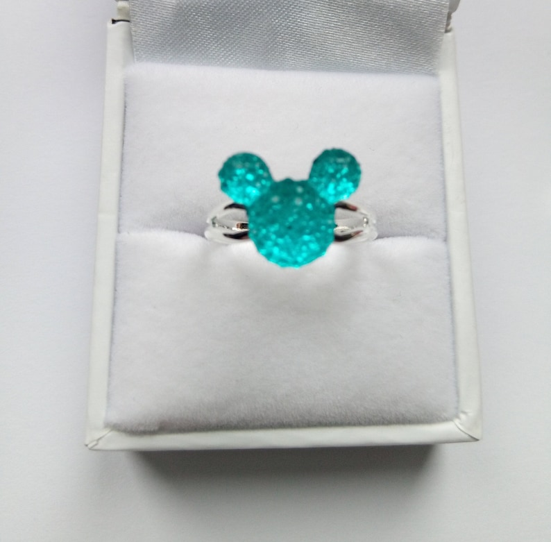 K&ouml;nnte beinhalten: Ein silberner Ring mit einem t&uuml;rkisblauen Mickey-Maus-Kopfdesign. Der Ring befindet sich in einer wei&szlig;en Ringbox.